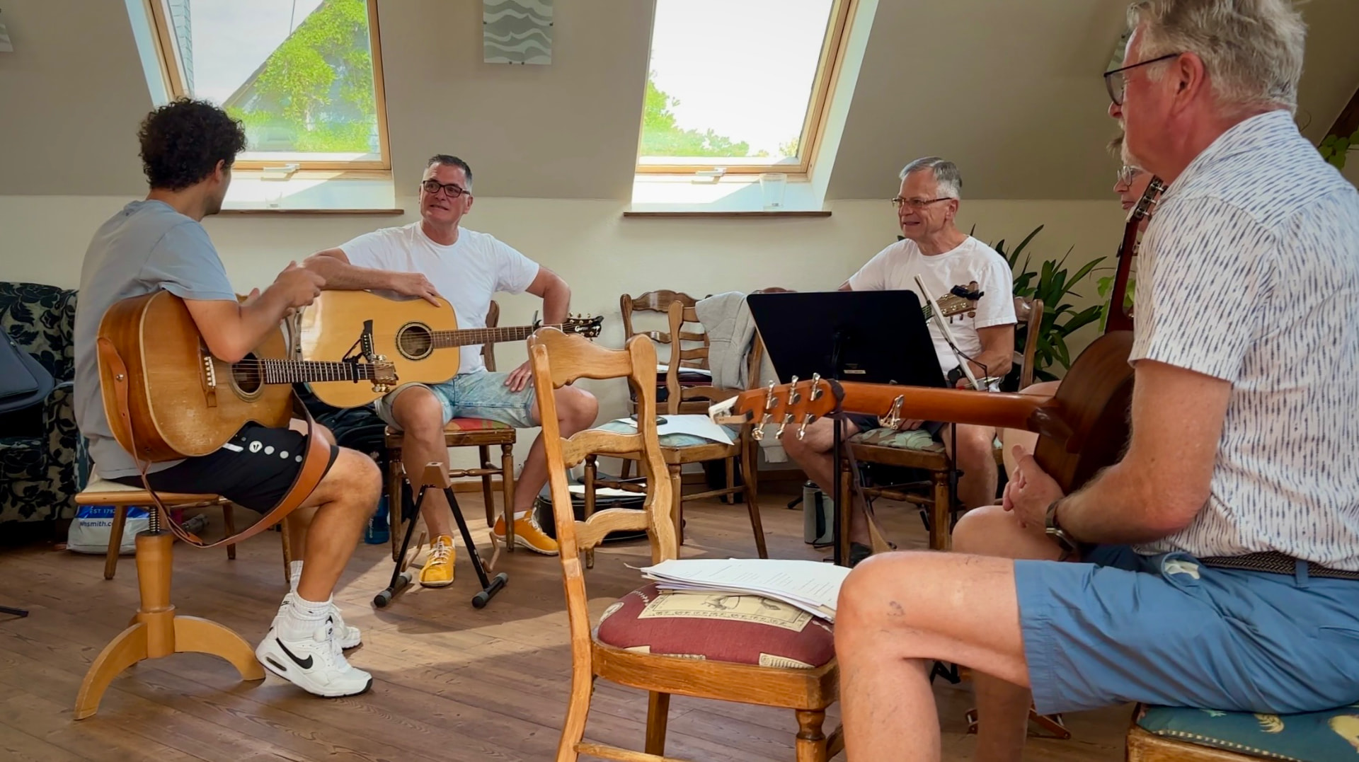 Teilnehmer sitzen im Kreis mit Akustikgitarren in einem hellen Raum mit Dachfenstern